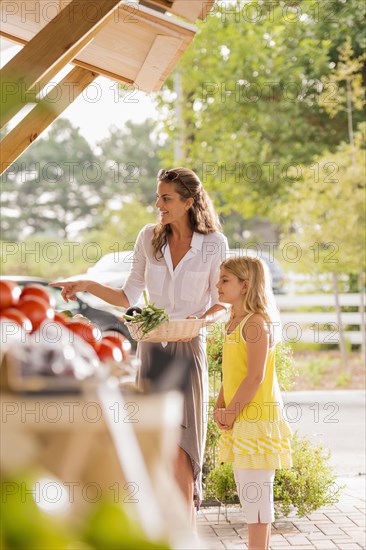 Mixed race mother and daughter browsing produce at farmers market