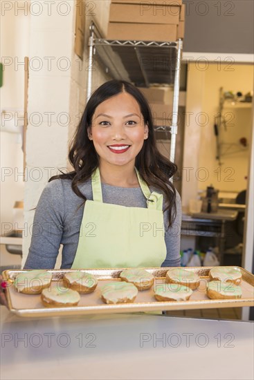 Asian baker holding tray of donuts in bakery