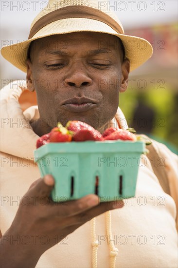 African American man examining basket of strawberries