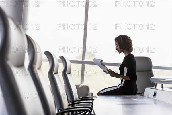 Black businesswoman sitting on conference table reading notepad