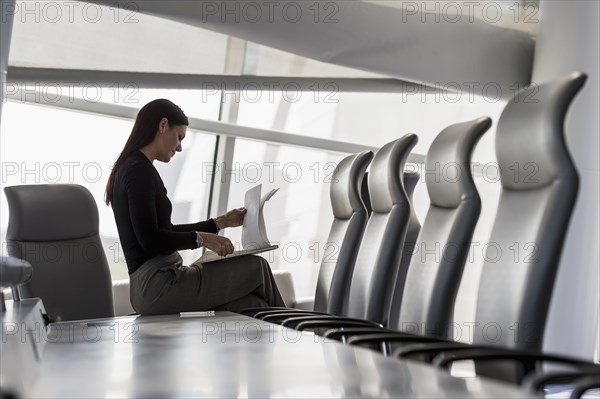 Caucasian businesswoman sitting on conference table reading notepad