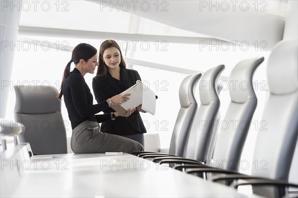 Caucasian businesswomen at conference table reading notepad