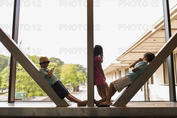 Caucasian boys and girl leaning on beams in airport