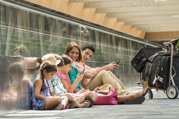 Family waiting on floor of airport using cell phones