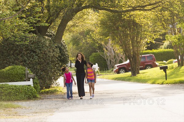 Mother walking in street with daughters wearing backpacks