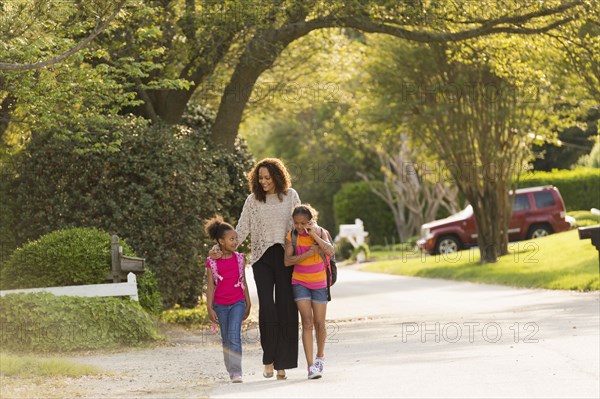 Mother walking in street with daughters wearing backpacks