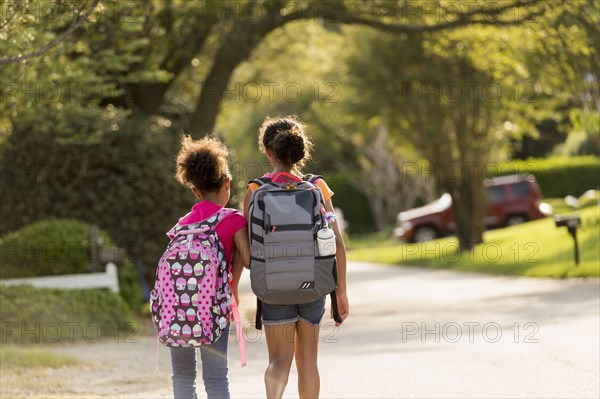 Sisters walking in street wearing backpacks