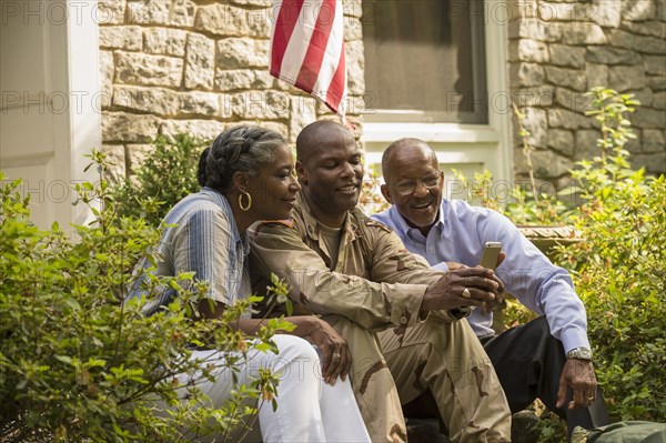 Soldier sitting on front stoop with parents and texting on cell phone