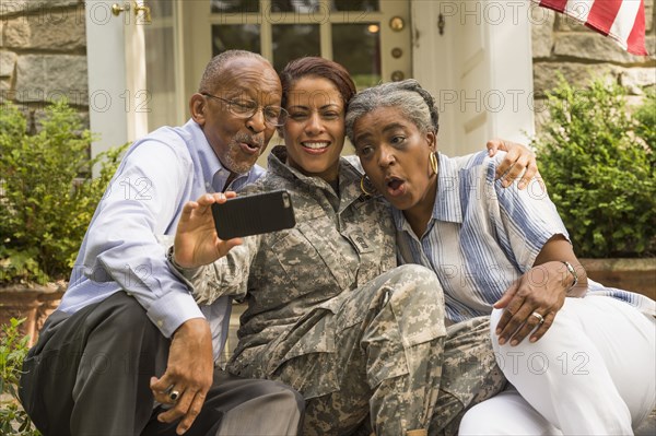 Soldier sitting on front stoop with parents and posing for cell phone selfie