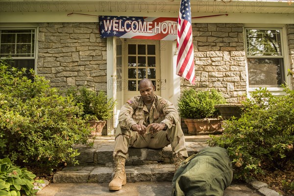 Frustrated African American soldier sitting on front stoop