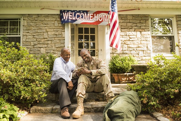 Soldier and father sitting on front stoop texting on cell phone