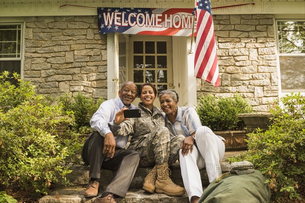 Soldier and parents sitting on front stoop posing for cell phone selfie