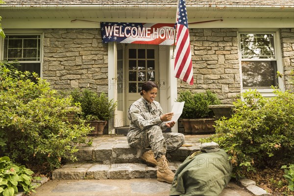 Smiling African American soldier sitting on front stoop reading letter