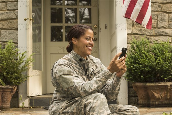 Smiling African American soldier sitting on front stoop texting on cell phone