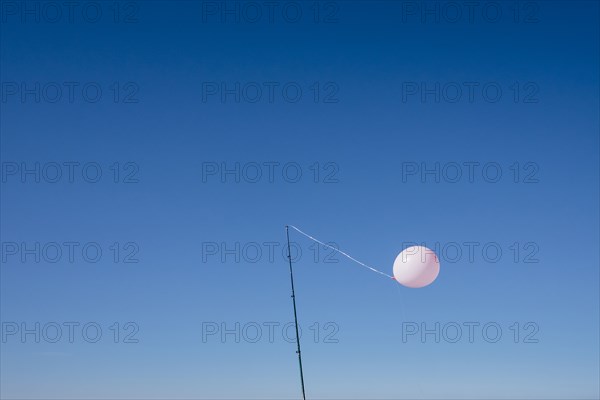 Balloon tied to pole in blue sky