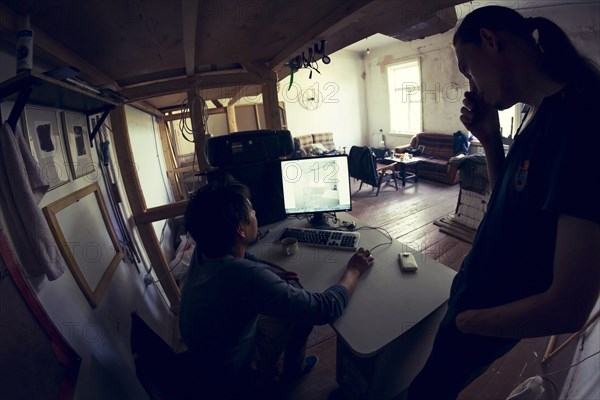 Young men using laptop together under loft bed