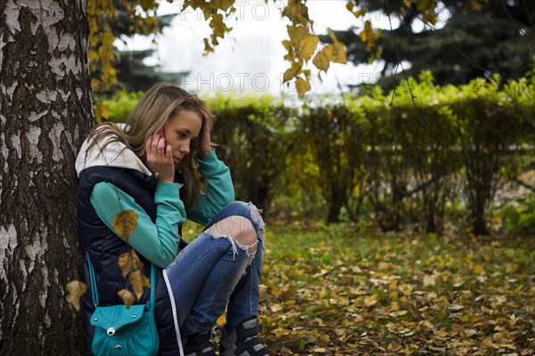 Caucasian woman talking on cell phone near tree