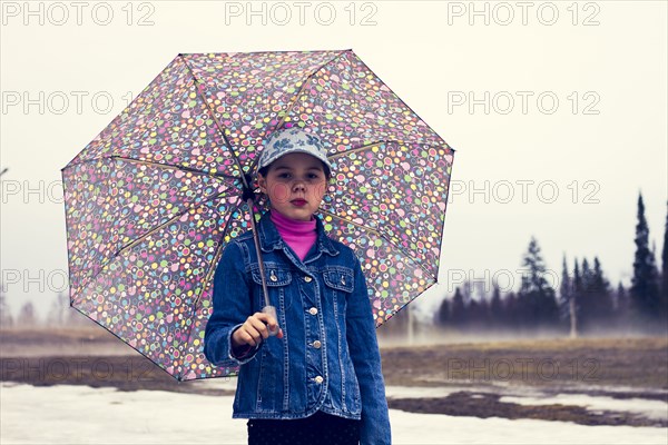 Caucasian girl walking under umbrella in snowy field