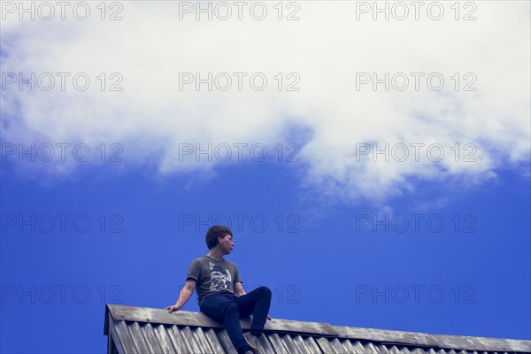Low angle view of Caucasian boy sitting on tin roof