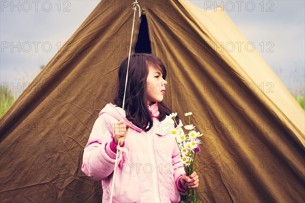 Caucasian girl holding wildflowers near camp tent