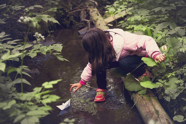 Caucasian girl floating paper boat on forest creek