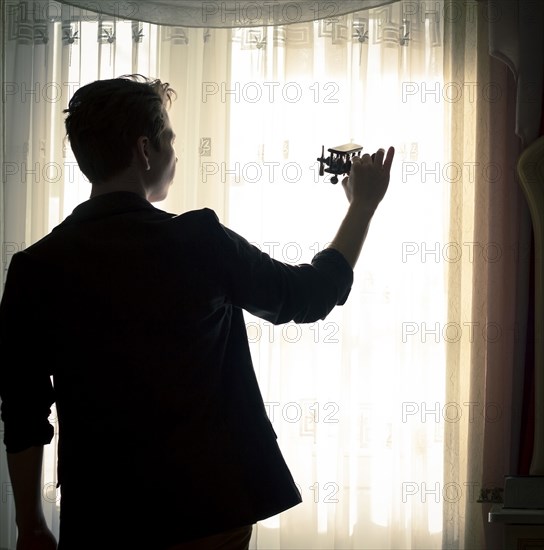 Caucasian man playing with toy airplane near window