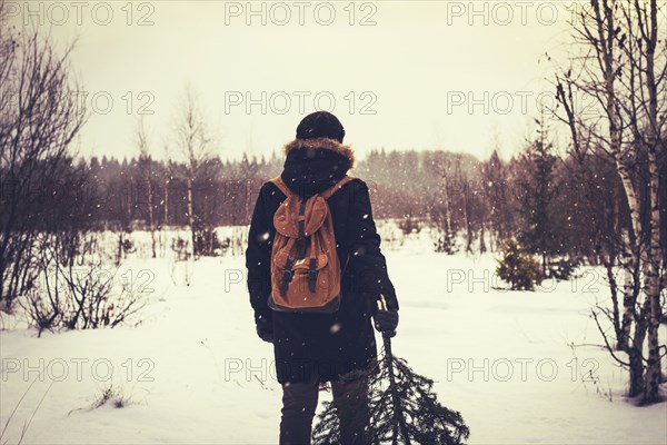 Caucasian man carrying tree in snowy field