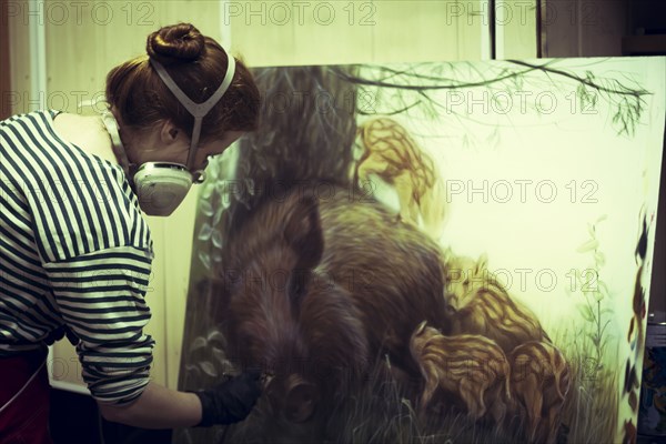 Artist in gas mask airbrushing painting in studio