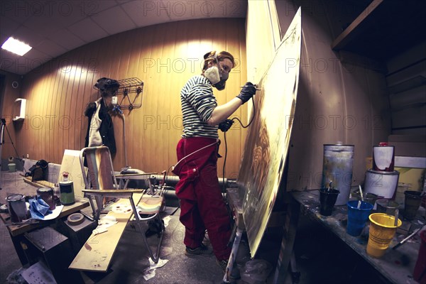 Artist in gas mask airbrushing painting in studio