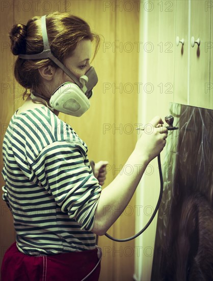 Artist in gas mask airbrushing painting in studio