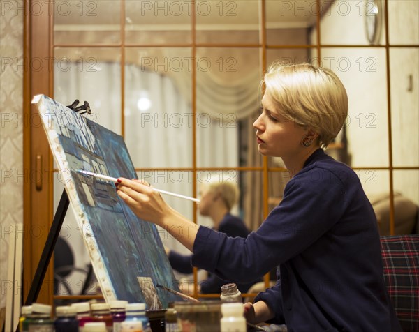 Caucasian woman painting on canvas near mirror