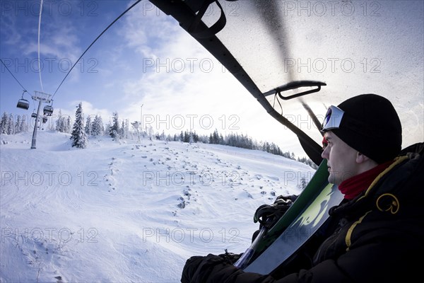 Caucasian snowboarder riding chair lift over snowy slopes