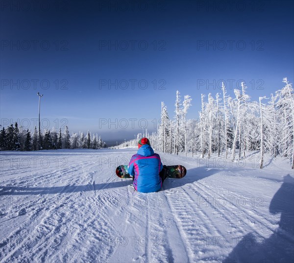 Caucasian snowboarder sitting on snowy slope
