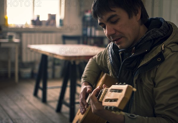 Asian man playing guitar in living room