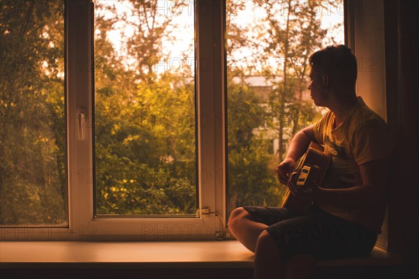 Caucasian man playing guitar in window sill