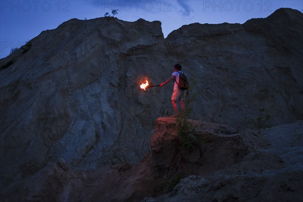 Caucasian man holding torch under rocky cliff