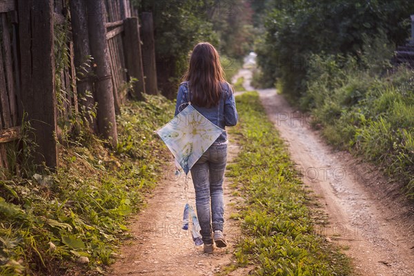 Caucasian teenage girl carrying kite on dirt road