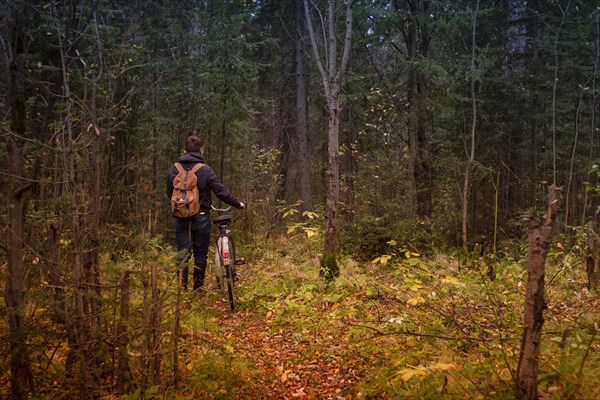 Caucasian man pushing bicycle on forest path