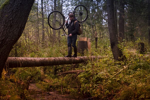 Caucasian man carrying bicycle on fallen tree