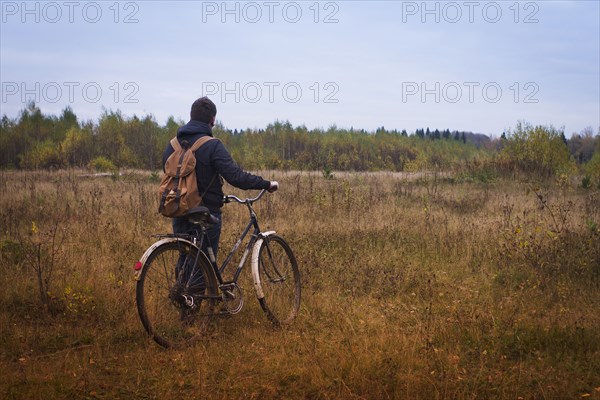 Caucasian man pushing bicycle in field