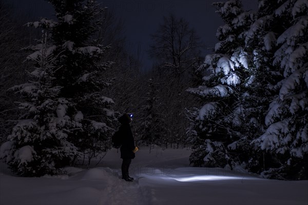 Caucasian hiker wearing headlamp in snowy forest