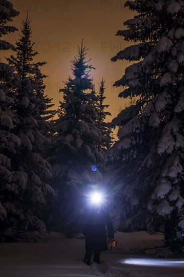 Caucasian hiker wearing headlamp in snowy forest