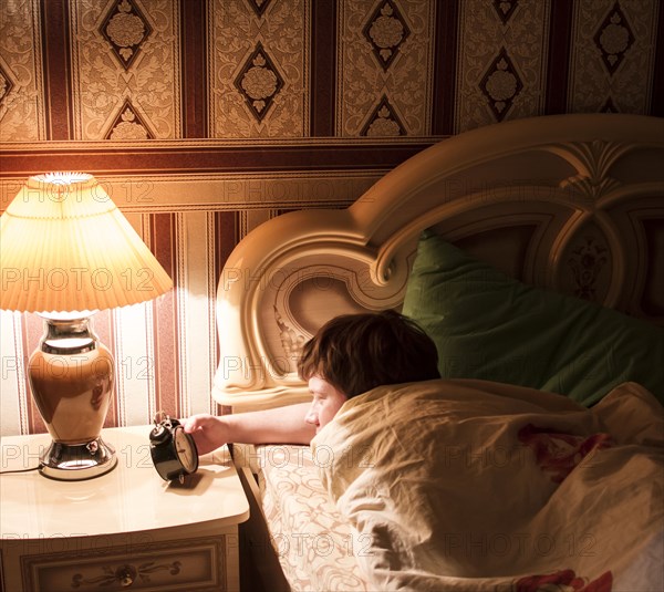 Caucasian man checking alarm clock in bed