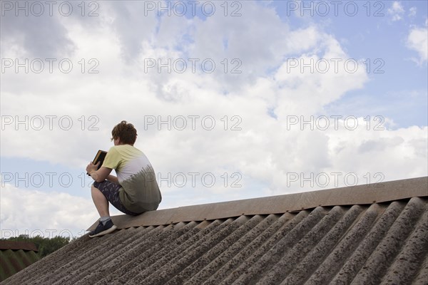 Caucasian man sitting on roof holding book