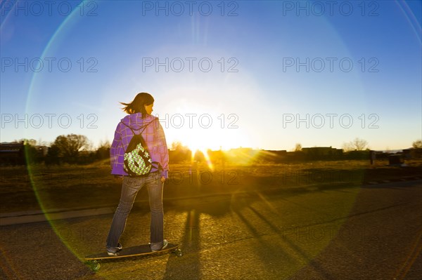 Chinese girl skateboarding on road at sunset