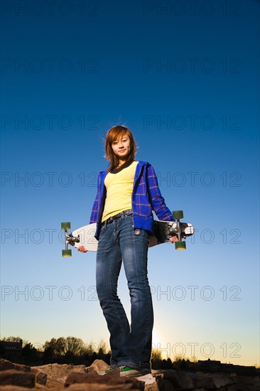 Chinese girl standing on rocks holding skateboard