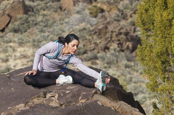 Hispanic woman stretching on rock