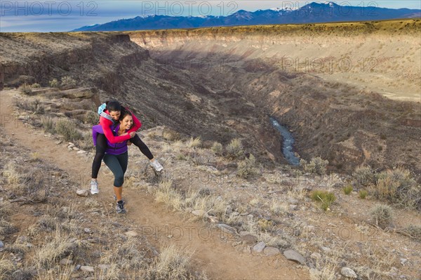 Hispanic woman carrying friend on her back in remote area