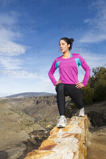 Hispanic woman stretching on rock wall in remote area