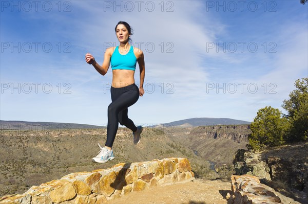 Hispanic woman jumping in mid-air in remote area